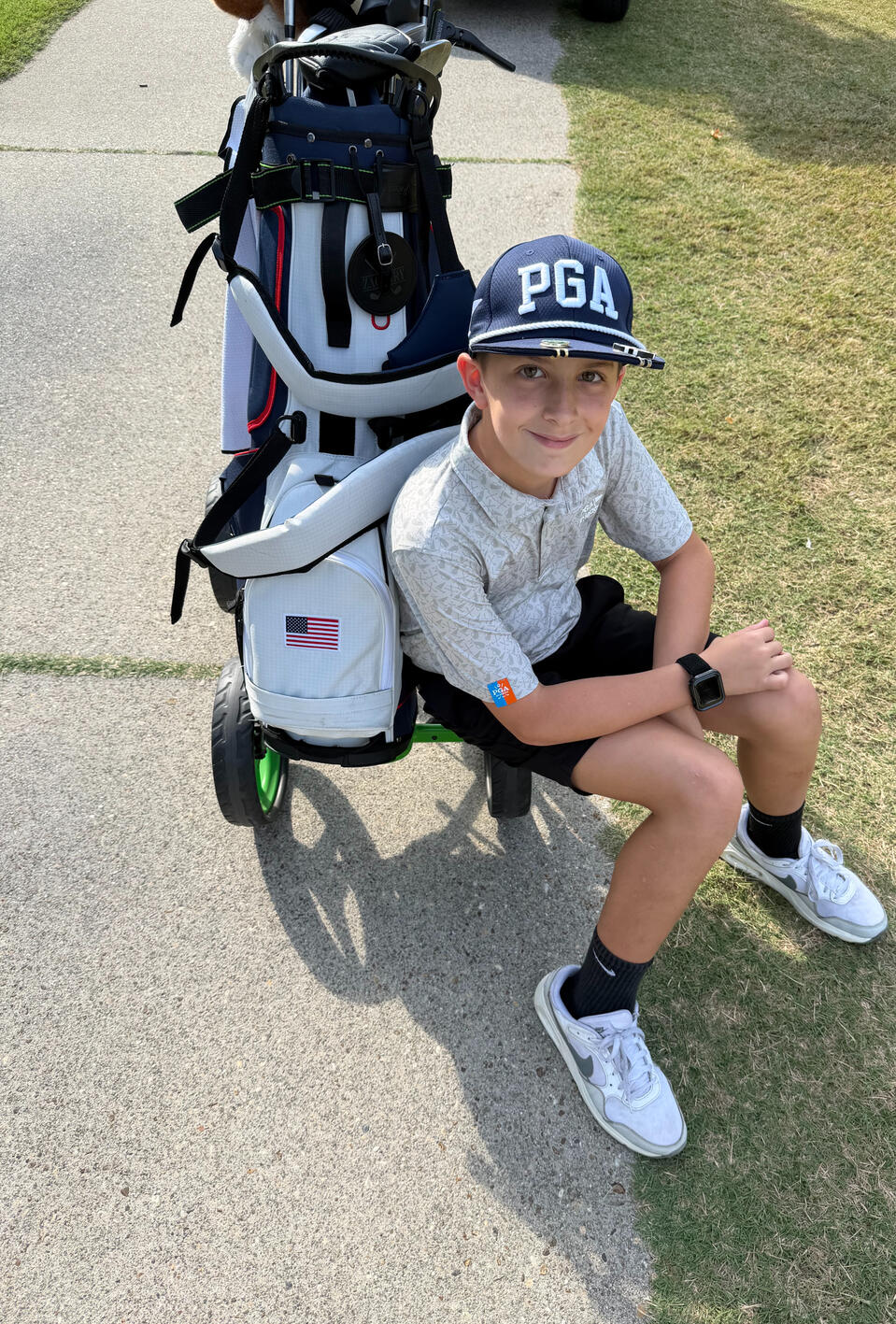 Zachary Walker sitting beside his golf bag at a golf course, wearing a PGA hat.